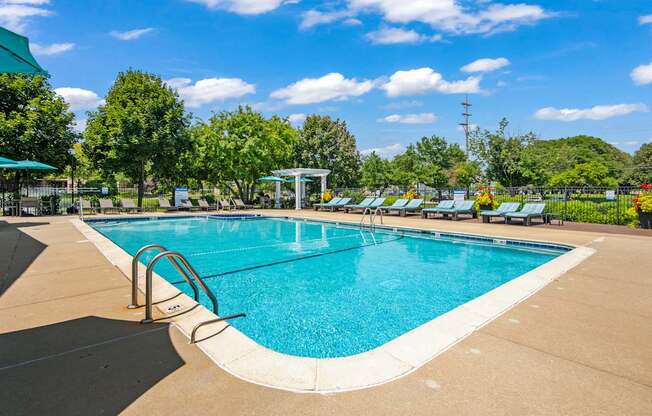 A large outdoor swimming pool surrounded by trees and a clear blue sky.