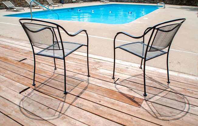 Two black chairs are on a wooden deck by a pool.