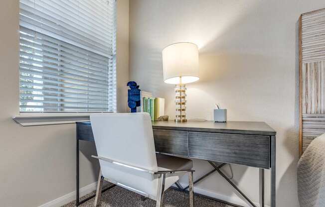 A white chair sits in front of a desk with a lamp on it.