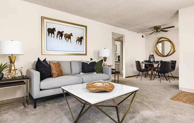 A living room with a grey couch, a coffee table, and a painting of horses.