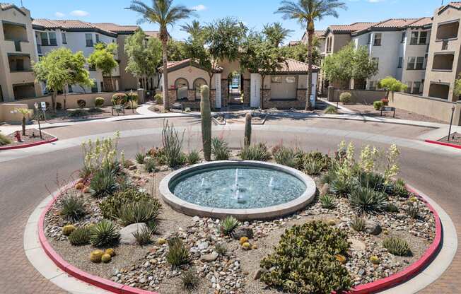 A fountain in the middle of a landscaped area with apartment buildings in the background.