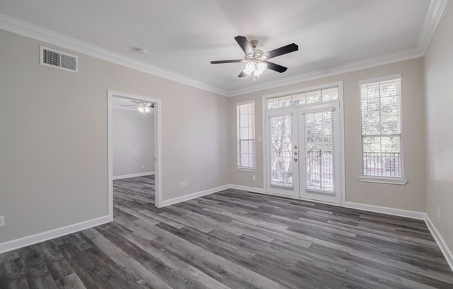 an empty living room with a ceiling fan and windows