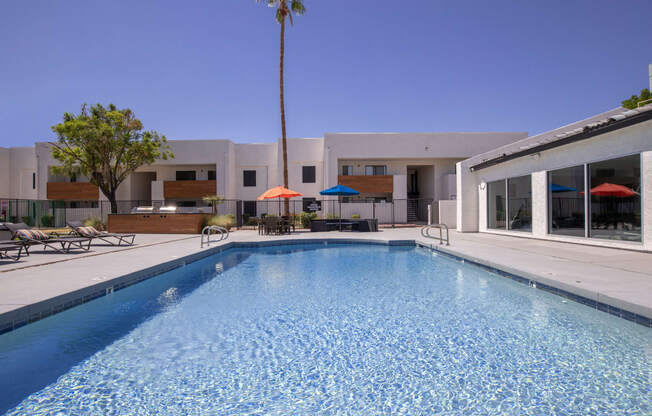 a large swimming pool with lounge chairs and umbrellas in front of a white building