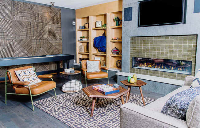 Cozy communal lounge in the apartment complex featuring stylish seating arrangements, a modern flat-screen TV, a warm fireplace, and a tabletop shuffleboard for residents to enjoy.