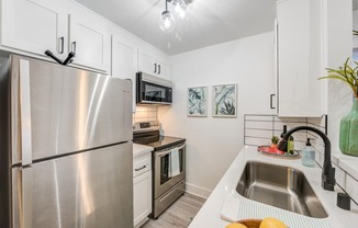 Fusion Warner Center apartment in Woodland Hills galley kitchen with stainless steel appliances, white cabinets, and white tile backsplash.