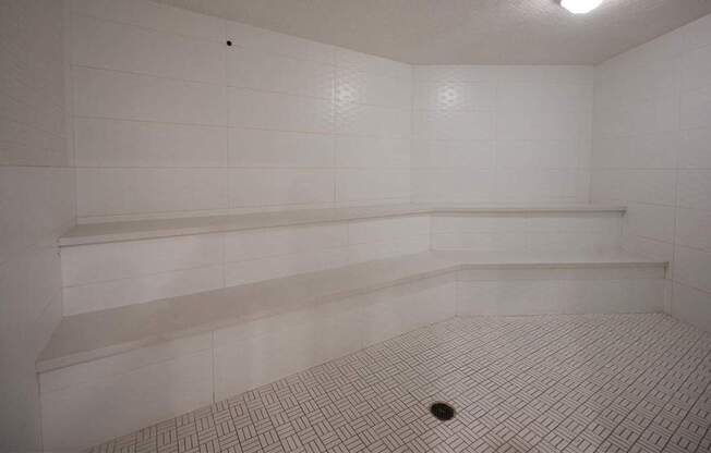 A white tiled room with a drain in the middle.