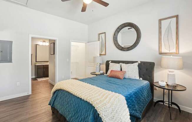 A bedroom with a bed, a mirror, a ceiling fan, and a side table.