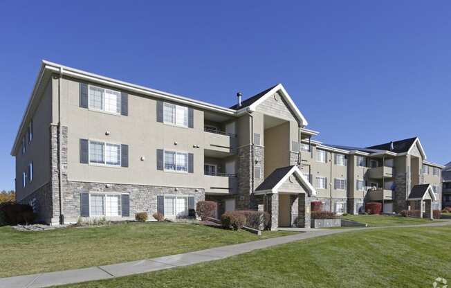 an exterior view of an apartment building with green grass and a sidewalk