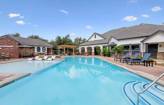 A large swimming pool with lounge chairs and a house in the background.