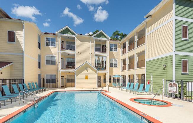 Sparkling resort-style swimming pool and hot tub with lounge chairs at Evergreens at Mahan apartments in Tallahassee, FL