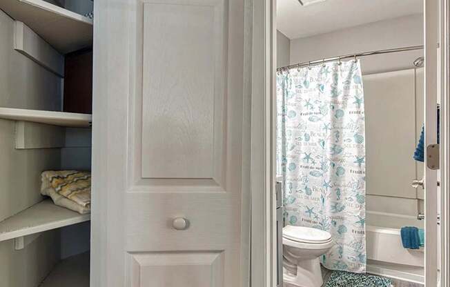 A white bathroom with a toilet, a shower curtain, and a towel on the shelf.