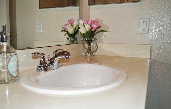 a white sink sitting next to a vase of flowers on a table