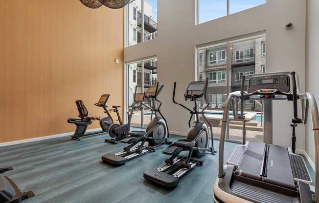 a gym with cardio equipment and a window overlooking a pool