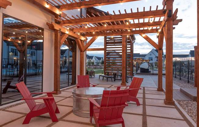 A wooden pergola with red chairs and a table is set up outside.