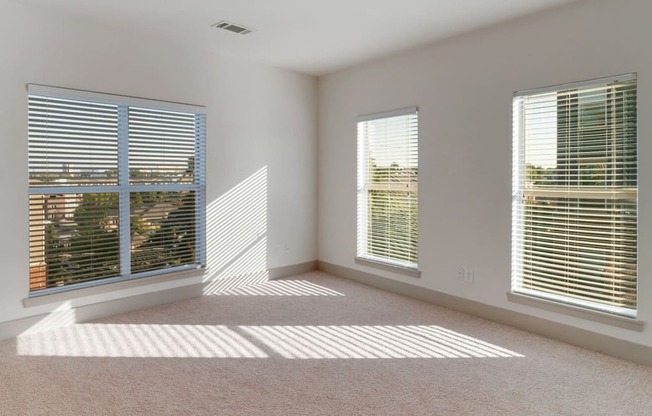 an empty living room with three windows and a carpet