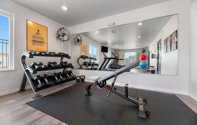 A gym with a row of dumbbells and a bench press.