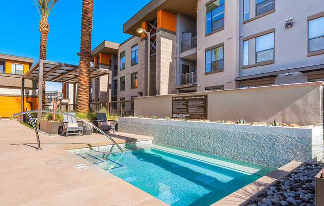 A pool surrounded by a stone wall and palm trees.