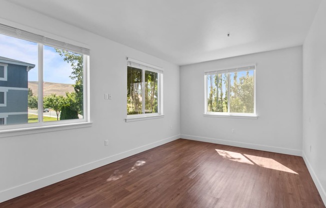 a bedroom with hardwood floors and three windows