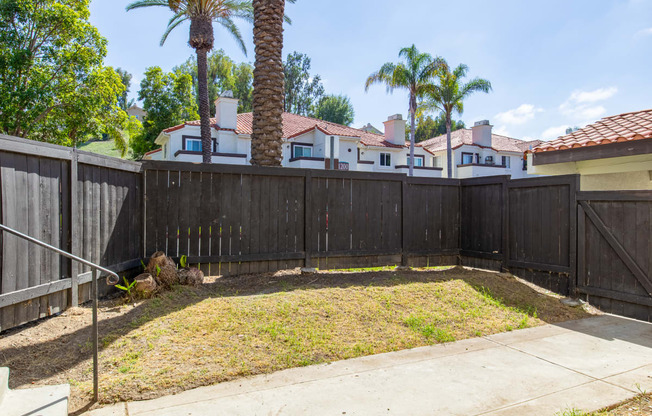 a fenced in yard with palm trees and a house in the background