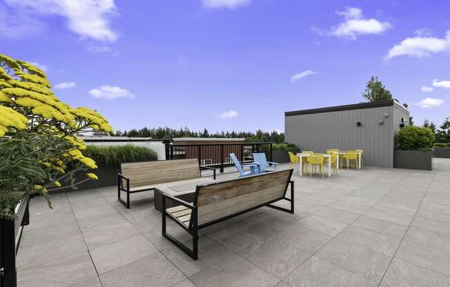 a roof terrace with a benches facing the cozy firepit with chairs and yellow flowers at Arabella Apartment Homes, WA 98155