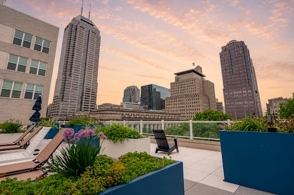 A rooftop garden with a chair and a table in the foreground and a city skyline in the background.