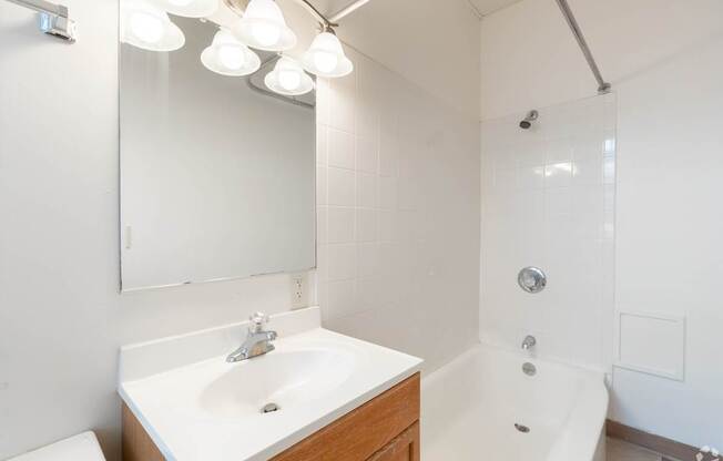A white bathroom with a sink, mirror, and tub.