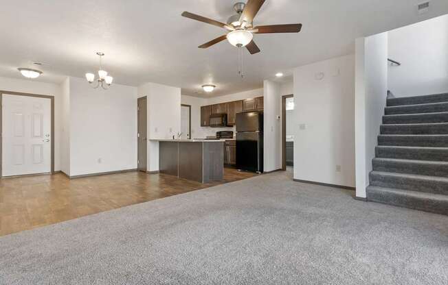 A living room with a grey carpet and a ceiling fan.
