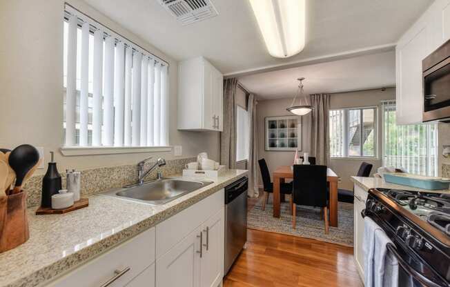 Kitchen with View of Dining Room with Wood Inspired Floor, Sink, Cupboards, Stove, Oven, Wooden Dining Room Table and Black Chairs