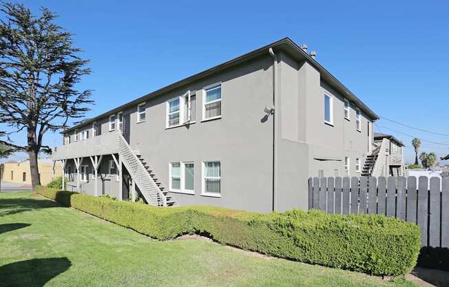 A grey house with a white picket fence and a tree in front.