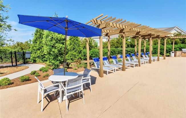 A row of lounge chairs and a picnic table on the pool sundeck near trees and bushes