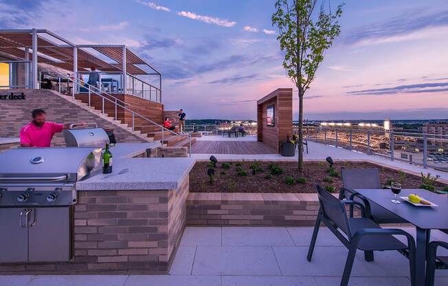 A woman in a pink shirt is standing on a patio with a grill.