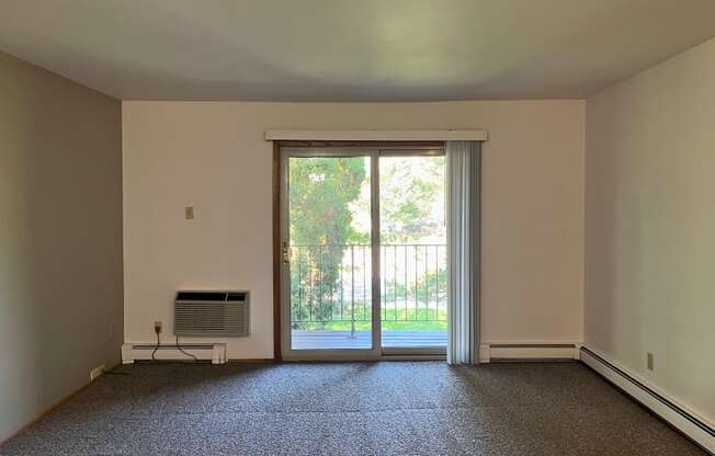 A room with a carpeted floor, a window with blinds, and a sliding glass door leading to a patio.