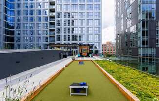 A green lawn with a table and chairs is in the foreground of a city scene.