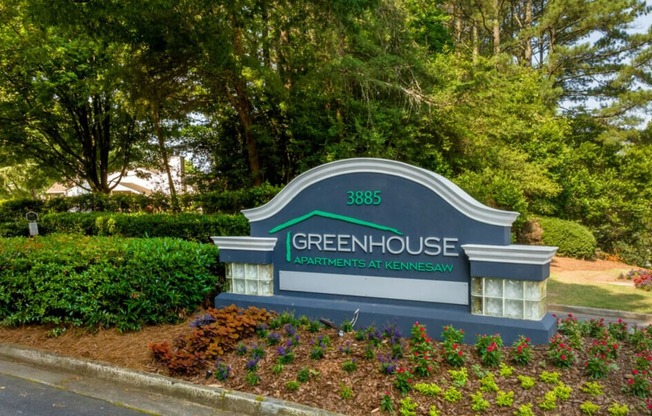 a sign that says green house with trees in the background
