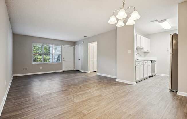 an empty living room with a kitchen in the background