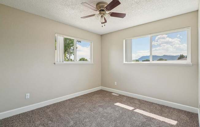A room with a ceiling fan and two windows.