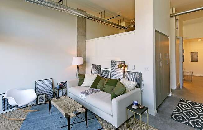 Apartment living room with staged couch, coffee table and rug. Concrete flooring and tall ceilings.at 19th & Mercer, Seattle, WA