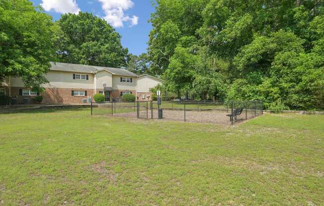 A grassy dog park with a fence and a house in the background.