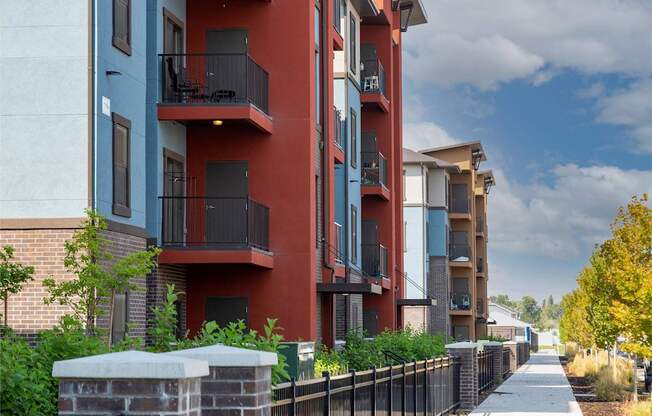A row of modern apartment buildings with balconies and a sidewalk in front.