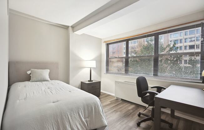 a bedroom with a bed and a desk and a large window