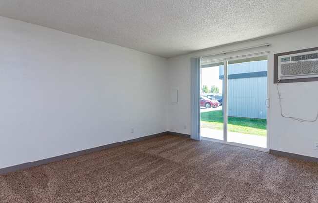 A room with a carpeted floor and a sliding glass door leading to a backyard.
