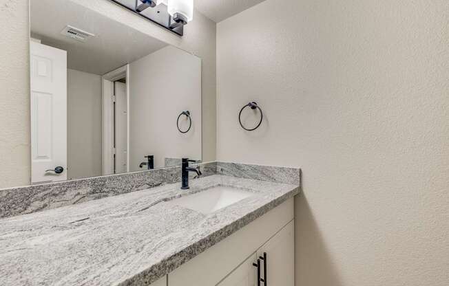 A bathroom with a marble countertop and a mirror above the sink.
