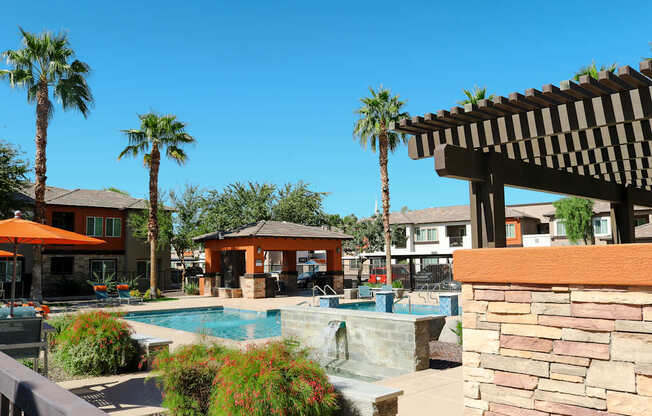 A pool area with a waterfall and a patio with a table and chairs.
