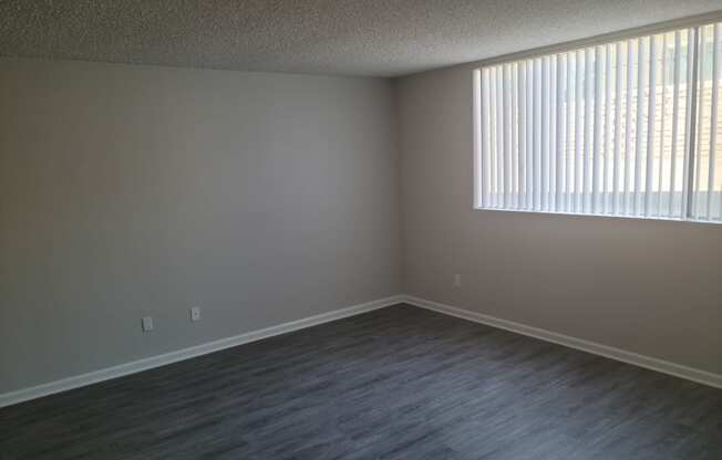 Living room with hardwood-style vinyl flooring and large window at La Mesa Village apartments.