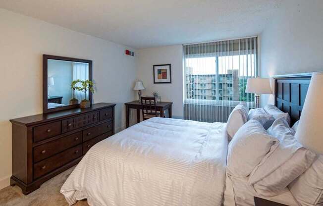 A bedroom with two beds, a dresser, and a window with blinds.