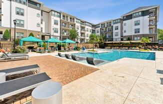 an outdoor pool with lounge chairs and umbrellas in front of an apartment building