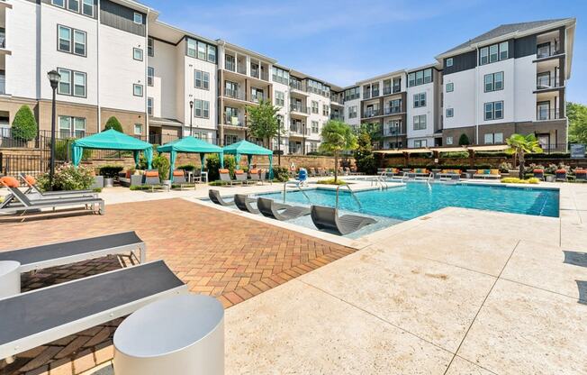 an outdoor pool with lounge chairs and umbrellas in front of an apartment building