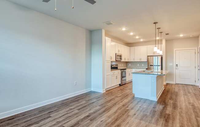 an empty living room with a kitchen with white cabinets at The Bella at Westchester, Virginia