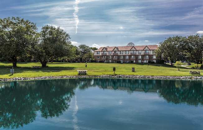 A serene landscape with a building, trees, and a calm lake.