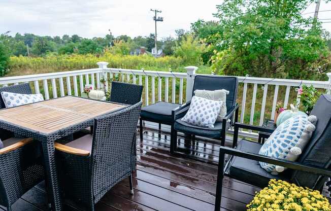A wooden table and two chairs are on a porch.